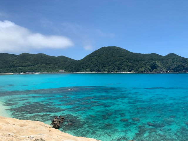 Image of a Mountain filled with greenery in front of a blue Ocean. - Aharen, Tokashiki, Shimajiri District, Okinawa, Japan - Aharen, Tokashiki, Shimajiri District, Okinawa, Japan